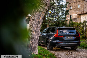 Volvo V60 – rear three-quarter, dark grey metallic on a gravel driveway by a stone tower