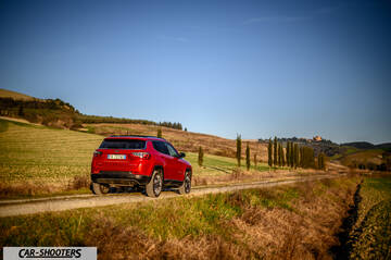 Jeep Compass – rear three-quarter, red on a dirt road through hills