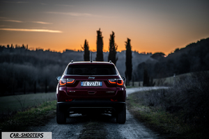 Jeep Compass – rear view, dark red on a dirt road at sunset