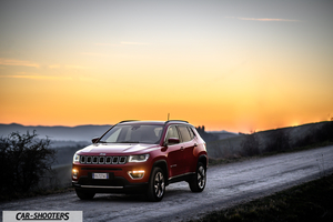 Jeep Compass – front three-quarter, red on a dirt road at sunset
