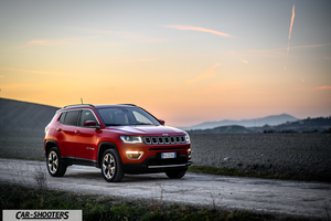 Jeep Compass – front three-quarter, red on a dirt road at sunset
