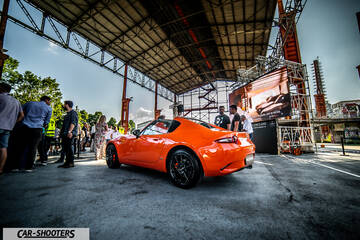 rear three-quarter, bright orange in an industrial event space