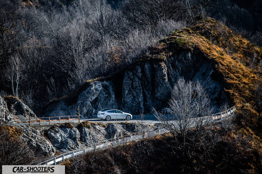Tesla Model 3 – rear three-quarter, white against a mountain backdrop