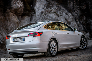 Tesla Model 3 – rear three-quarter, pearl white against a rock face backdrop