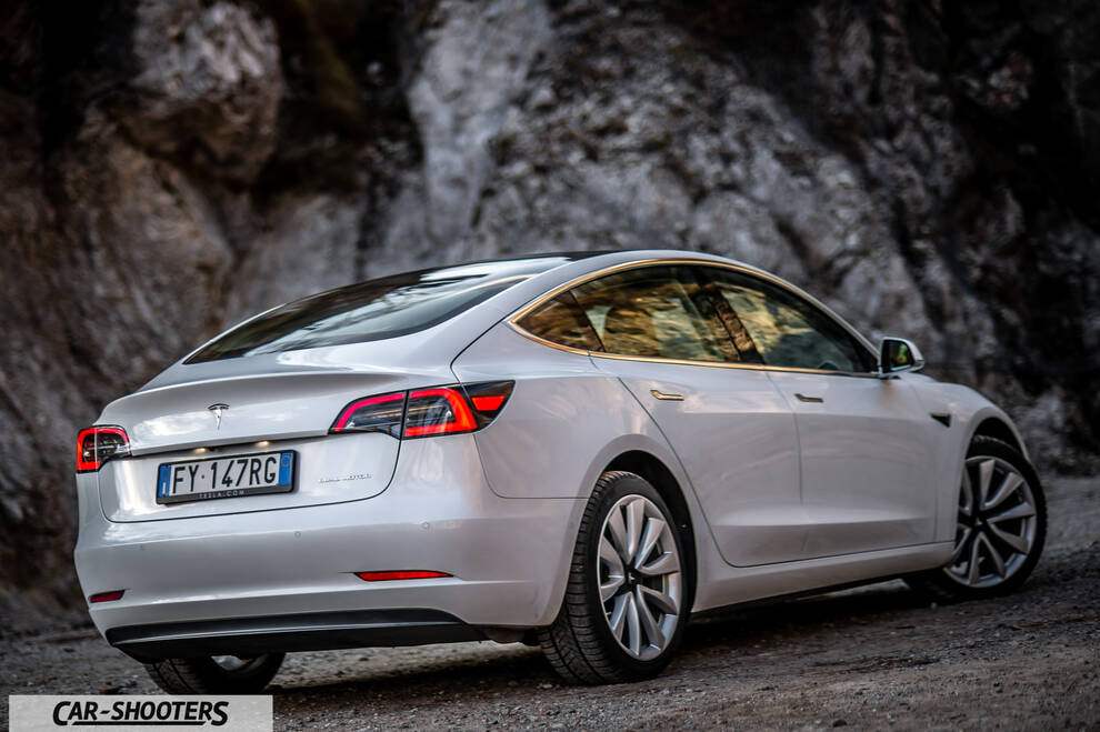 Tesla Model 3 – rear three-quarter, pearl white against a rock face backdrop