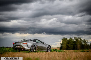 Lexus LC500h – rear three-quarter, silver in a grassy field under a stormy sky