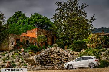 Mercedes Benz Classe B – side profile, white against a rustic stone building backdrop