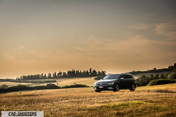 Volkswagen Passat Alltrack – front three-quarter, dark grey against a rustic countryside landscape
