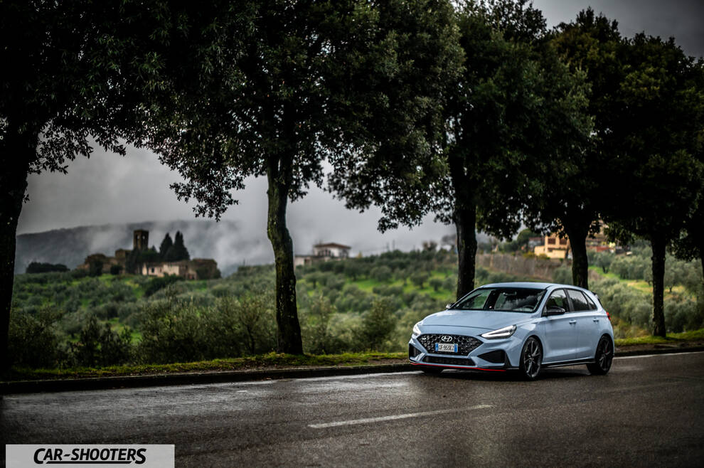 Hyundai i30N – front three-quarter, light blue on a wet road lined with trees