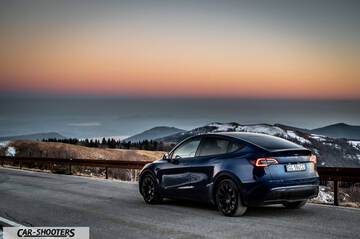 Tesla Model Y – rear three-quarter, dark blue against a mountain backdrop