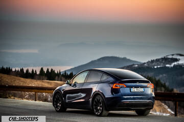 Tesla Model Y – rear three-quarter, dark blue against a mountain backdrop