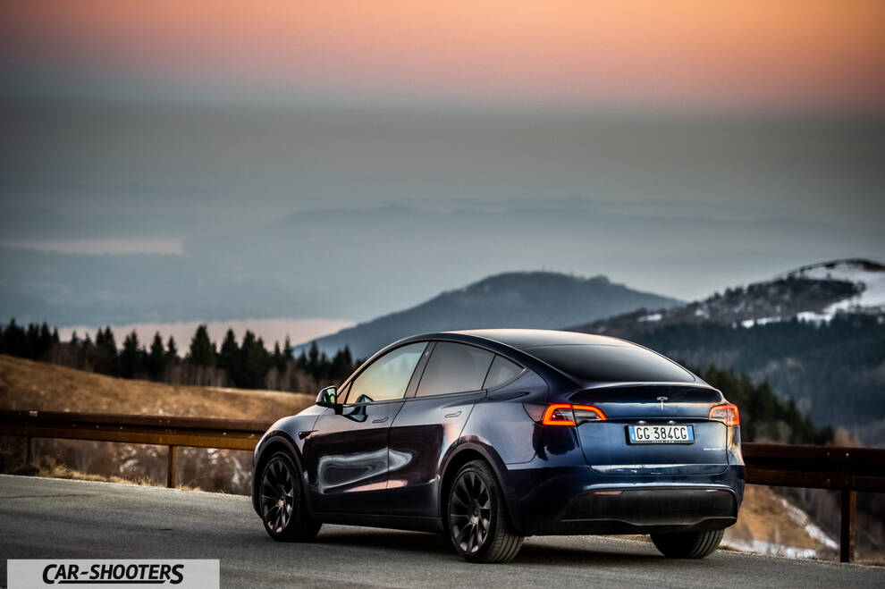 Tesla Model Y – rear three-quarter, dark blue against a mountain backdrop