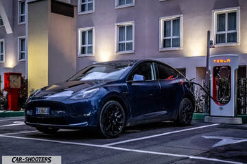 Tesla Model Y – front three-quarter, dark blue at a charging station