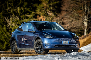 Tesla Model Y – front three-quarter, blue against a wooded backdrop with snow