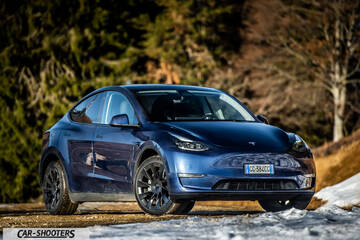Tesla Model Y – front three-quarter, blue against a wooded backdrop with snow