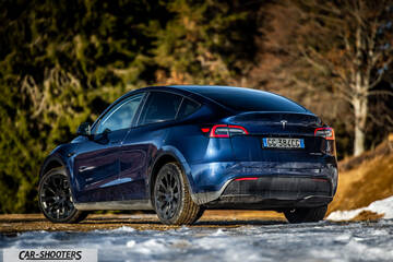 Tesla Model Y – rear three-quarter, blue metallic against a snowy forest backdrop