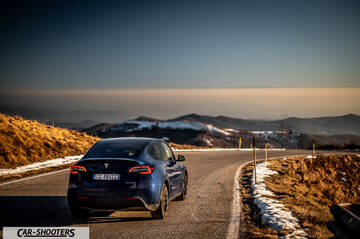 Tesla Model Y – rear three-quarter, blue metallic on a winding mountain road
