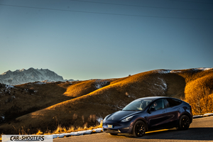 Tesla Model Y – front three-quarter, dark blue against a mountain backdrop