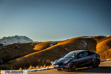 Tesla Model Y – front three-quarter, dark blue against a mountain backdrop
