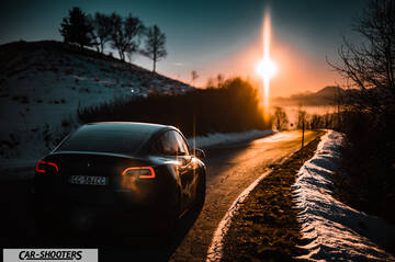 Tesla Model Y – rear three-quarter, black on a snowy country road at sunset