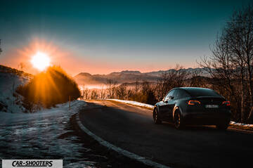 Tesla Model Y – rear three-quarter, dark grey on a mountain road at sunset