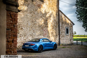 Alpine A110 – rear three-quarter, blue metallic against a rustic stone building