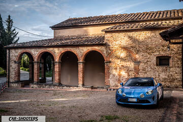 Alpine A110 – front three-quarter, blue metallic parked against a rustic stone building