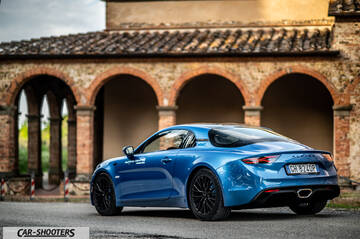Alpine A110 – rear three-quarter, blue metallic against an old stone building