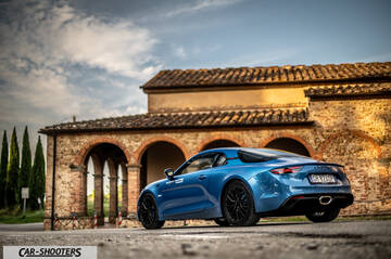 Alpine A110 – rear three-quarter, blue against an old stone building
