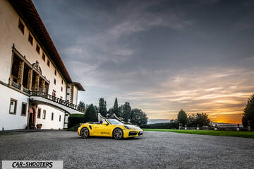 Porsche 911 Turbo Cabrio – front three-quarter, yellow parked near a large building at sunset