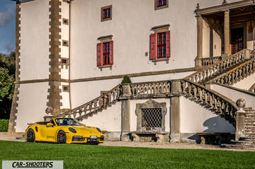 Porsche 911 Turbo Cabrio – front three-quarter, yellow in front of a historic building