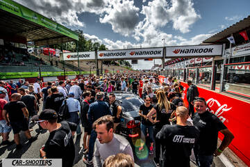 rear three-quarter, black at a crowded racetrack paddock