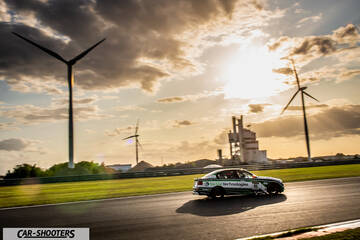 rear three-quarter, green on a racetrack with wind turbines