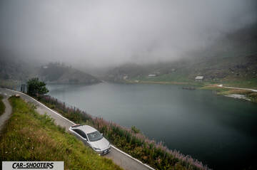 Hyundai Ioniq 6 – front three-quarter, silver on a mountain road next to a lake