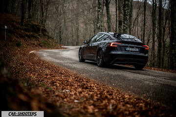 Tesla Model 3 2025 – rear three-quarter, dark grey on a winding forest road