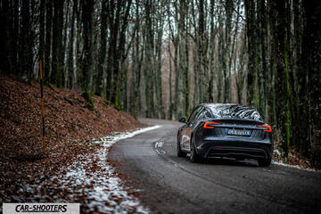 Tesla Model 3 2025 – rear three-quarter, dark grey on a winding forest road