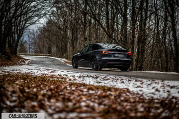 Tesla Model 3 2025 – rear three-quarter, dark grey on a winding winter road