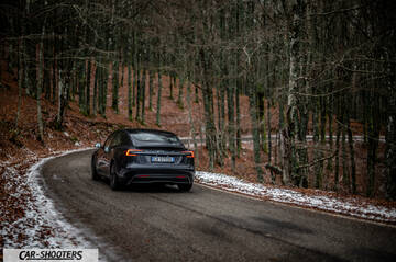 Tesla Model 3 2025 – rear three-quarter, dark grey on a winding forest road