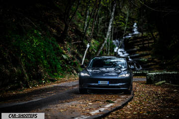 Tesla Model 3 2025 – front three-quarter, dark grey on a forest road with a waterfall backdrop