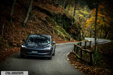 Tesla Model 3 2025 – front three-quarter, dark grey metallic on a winding country road