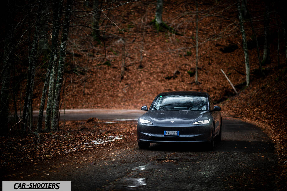 Tesla Model 3 2025 – front three-quarter, grey metallic on a winding forest road
