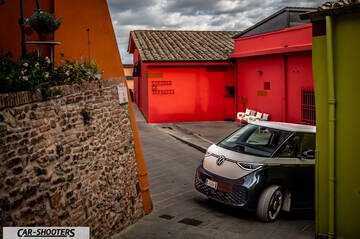 Volkswagen ID BUZZ – front three-quarter, dark grey and white on a narrow street between colorful buildings