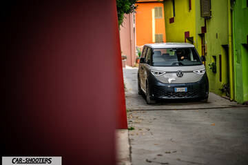 Volkswagen ID BUZZ – front three-quarter, silver and dark grey on a narrow street between colorful buildings