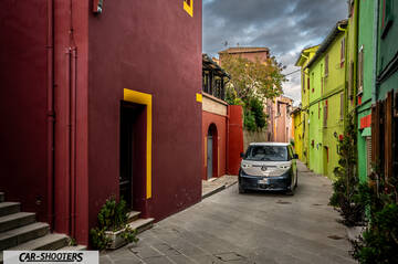 Volkswagen ID BUZZ – front three-quarter, silver in a colorful narrow street
