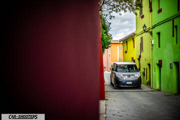 Volkswagen ID BUZZ – front three-quarter, grey and white on a narrow street between colorful buildings