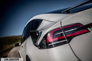 Tesla Model X – rear three-quarter, white with open charge port on a road