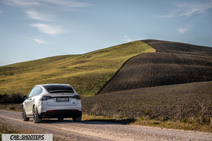 Tesla Model X – rear three-quarter, white against a rolling hill backdrop