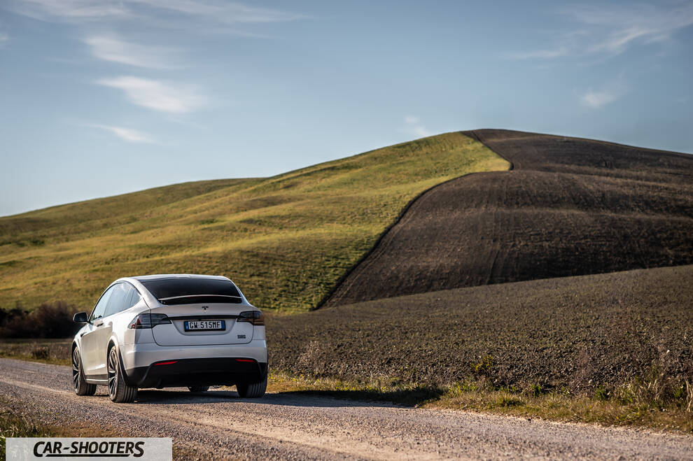 Tesla Model X – rear three-quarter, white against a rolling hill backdrop