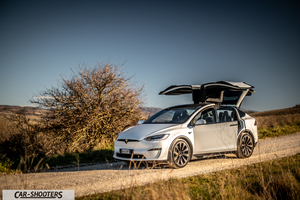 Tesla Model X – front three-quarter, white on a dirt road with falcon doors open