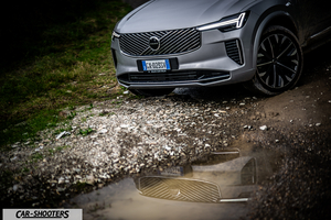 Volvo XC90 2025 – front three-quarter, silver on a gravel path with puddle reflection